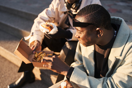 Focused happy guys eating burgers and enjoying taste at urban street