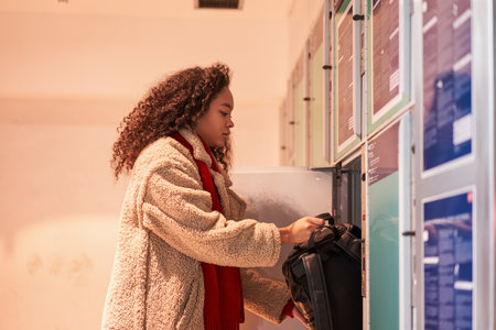 Multiracial female visitor in casual wear putting luggage in lockerの写真素材