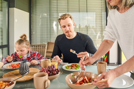 Careful grandmother lovingly imposes salad to her plateの写真素材