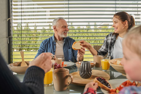 Cheerful woman giving bread to her senior father during the breakfastの写真素材