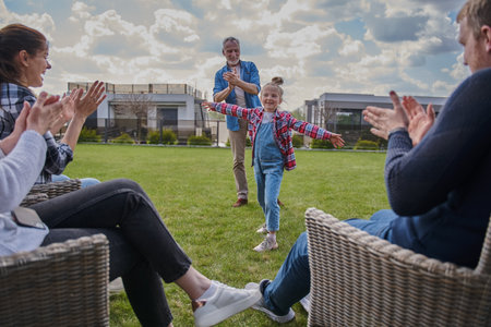 Happy family of three generations clapping hands while little girl standing with spread arms