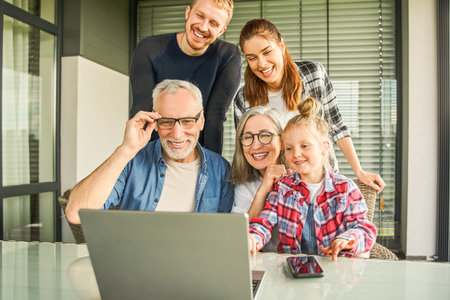 Happy family watching together video online in a laptop while sitting at homeの写真素材