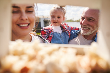 Smiling grandfather holding cute little girl in his arms while standing near birdhouseの写真素材