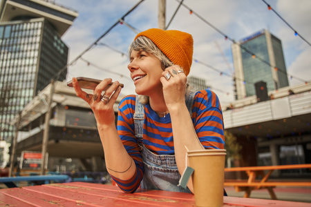 Adult happy woman recording voice message using smartphone at the street cafeの写真素材