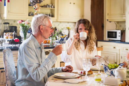 Happy caucasian family of senior father and daughter having breakfast in kitchen togetherの写真素材