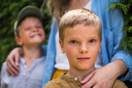 Blonde boy standing at the street near his mother and laughing brother and looking at the cameraの写真素材