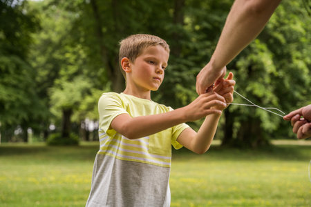 Unknown careful woman helping to her son making kite while standing at the grassの写真素材