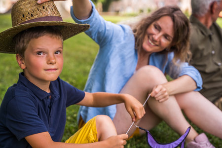 Cheerful mother putting hat at the head of her child while posing during the summerの写真素材