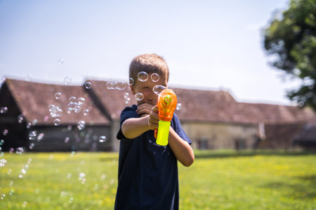 Little active boy holding soap bubbles gun and blowing bubbles at the cameraの写真素材