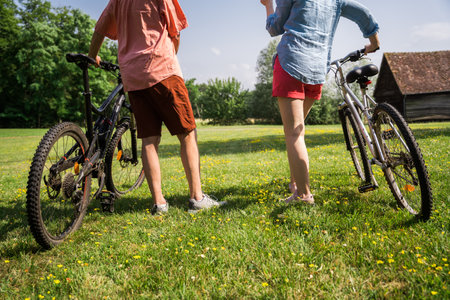 Close up shot of senior man and his adult daughter standing with bicycle in the grassの写真素材