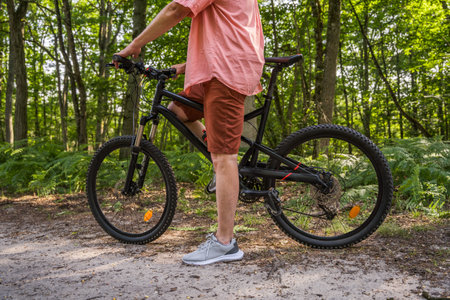Cropped shot of the mature man standing with bicycle in the forest road at the summerの写真素材