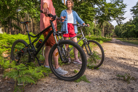 Full length of senior man and his daughter talking at the forest path with their bicyclesの写真素材