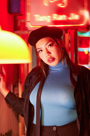 Vertical view of the hipster girl in stylish clothes standing on neon light wallsの写真素材