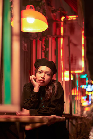 Vertical view of the young stylish brunette sitting in cafe in lights of night cityの写真素材