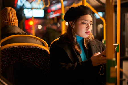 Teen asian woman in black hat messaging on smartphone at the busの写真素材