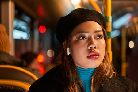 Serious asian woman ride in public transport bus or tram and listening music at the eveningの写真素材