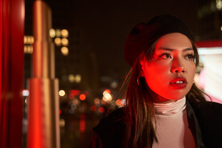 Stylish cool fashion funky asian young hipster girl posing near red neon street in nightの写真素材