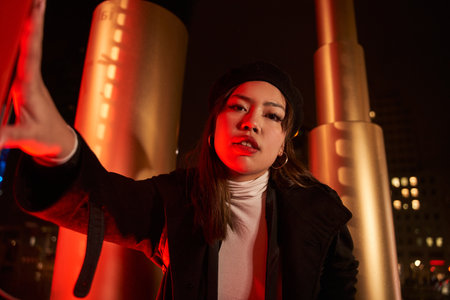 Portrait of young beautiful asian woman walking down city street illuminated neon night lightsの写真素材