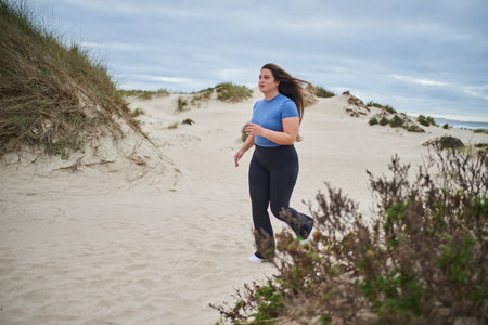 Young body positive sports woman running along the sandy sea shoreの写真素材