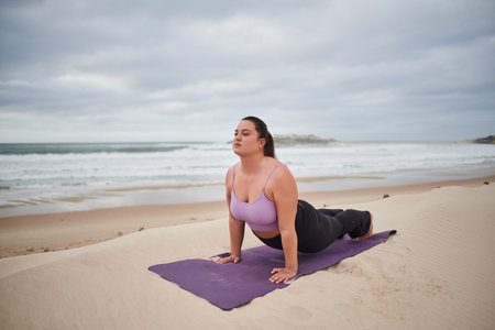 Body positive woman wearing sport clothes stretching in cobra pose on yoga matの写真素材