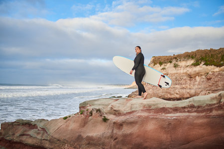Full length view of the caucasian woman walking with surfboard at the rocky hillの写真素材