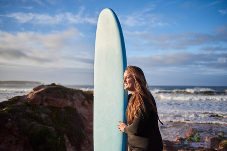 Long haired overweight female surfer posing with surf board in front of the ocean