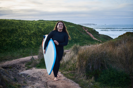 Professional female surfer holding surf board and walking through the hillの写真素材