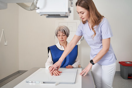 Female physician examining hand of senior lady and making joints x ray shoot at the clinicの写真素材