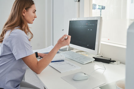 Lady doctor sitting computer workplace and holding special device for making x rayの写真素材