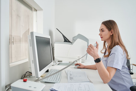 Lady doctor sitting computer workplace and holding special device for making x rayの写真素材