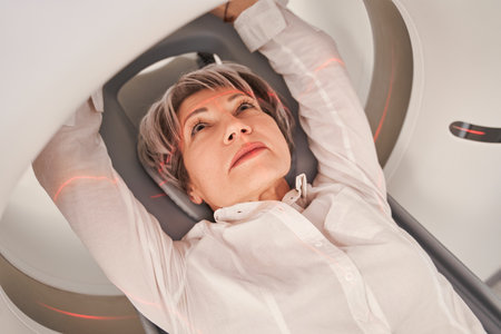 Mature female patient laying on bed while nurse preparing to X-ray on modern machineの写真素材