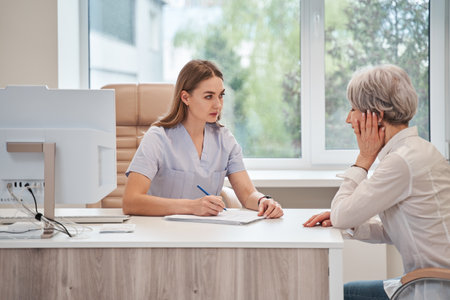 Female nurse talking and supporting old lady patient sitting at the table in hospitalの写真素材
