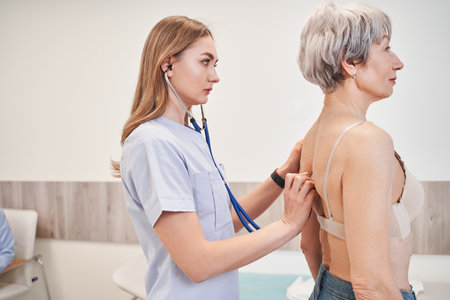 Experienced practitioner standing behind the patient and carefully listening to her lungsの写真素材