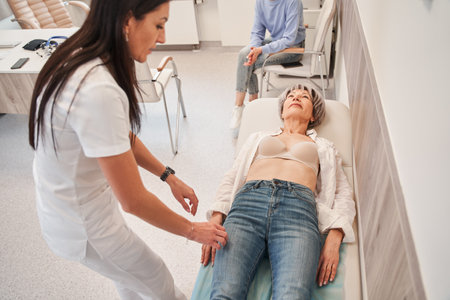 Female doctor in white coat palpating belly of senior woman lying on couchの写真素材