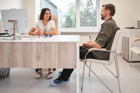 Happy smiling doctor and man patient sitting at the table and talking during medical check upの写真素材