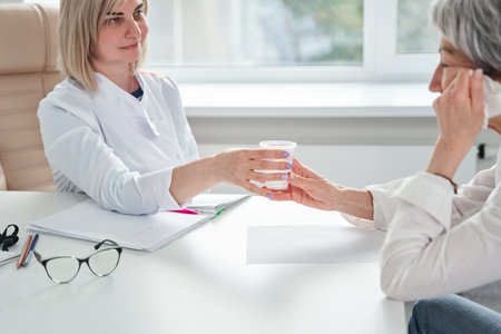Friendly doctor giving cup of water to her senior patient woman during sessionの写真素材