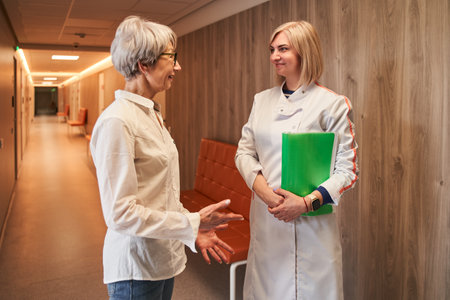 Doctor and senior woman patient discussing treatment at hospital corridorの写真素材