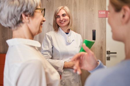 Senior woman and her daughter standing with doctor in clinic lobby after appointmentの写真素材