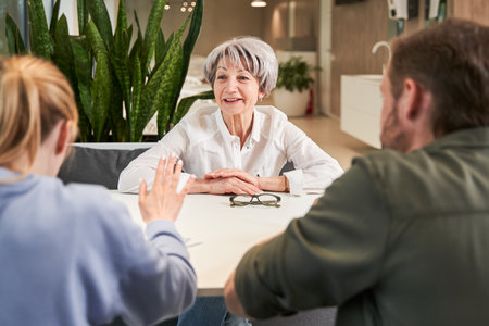 Smiling senior woman and her adult kids sitting and talking at the hospital tableの写真素材