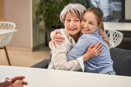 Joyful mature woman and her adult daughter embracing at the clinic tableの写真素材