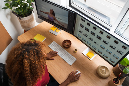 Young creative woman work on phone and computers editing photos at cozy home officeの写真素材