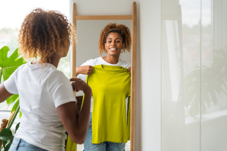 Cheerful african american woman trying on clothes and looking at the mirrorの写真素材