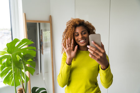 Multiracial happy woman video calling smartphone and looking awayの写真素材