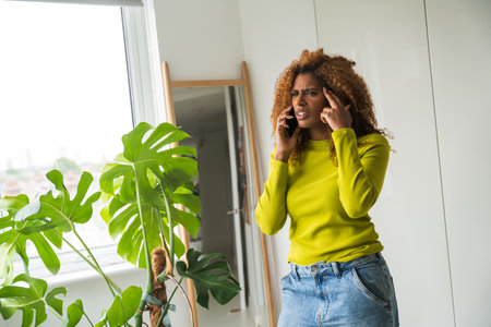 Nervous african american woman talking smartphone near the mirrorの写真素材