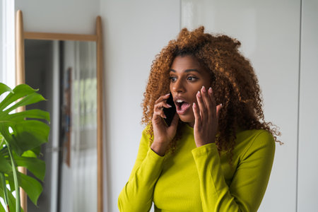 Surprised african american woman talking smartphone near the mirrorの写真素材