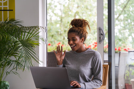 Cheerful pretty lady using laptop to chat with friend online at living roomの写真素材