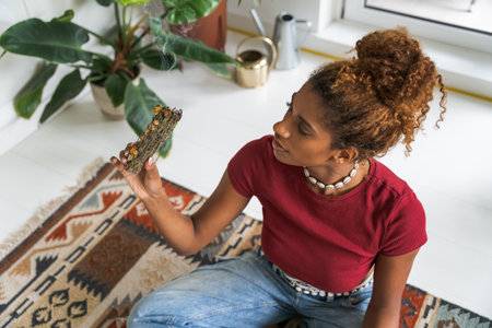 Gracious young woman holding santa palo wood and doing meditation in cozy roomの写真素材