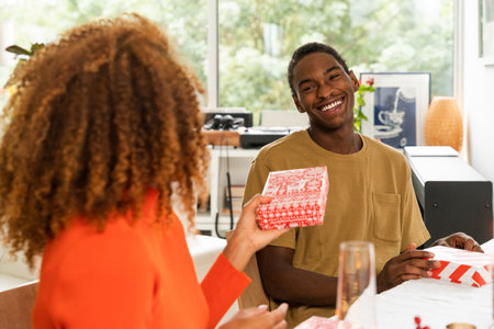 Curly woman presenting gift to her happy boyfriend at the Christmas tableの写真素材