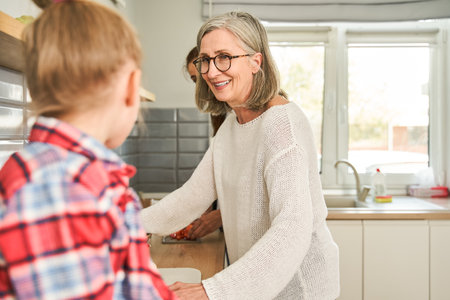 Smiling mature woman in eyeglasses looking at little girl while enjoying time at the kitchenの写真素材