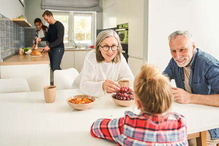 Cute grandmother and grandfather talking with little girl during the breakfastの写真素材